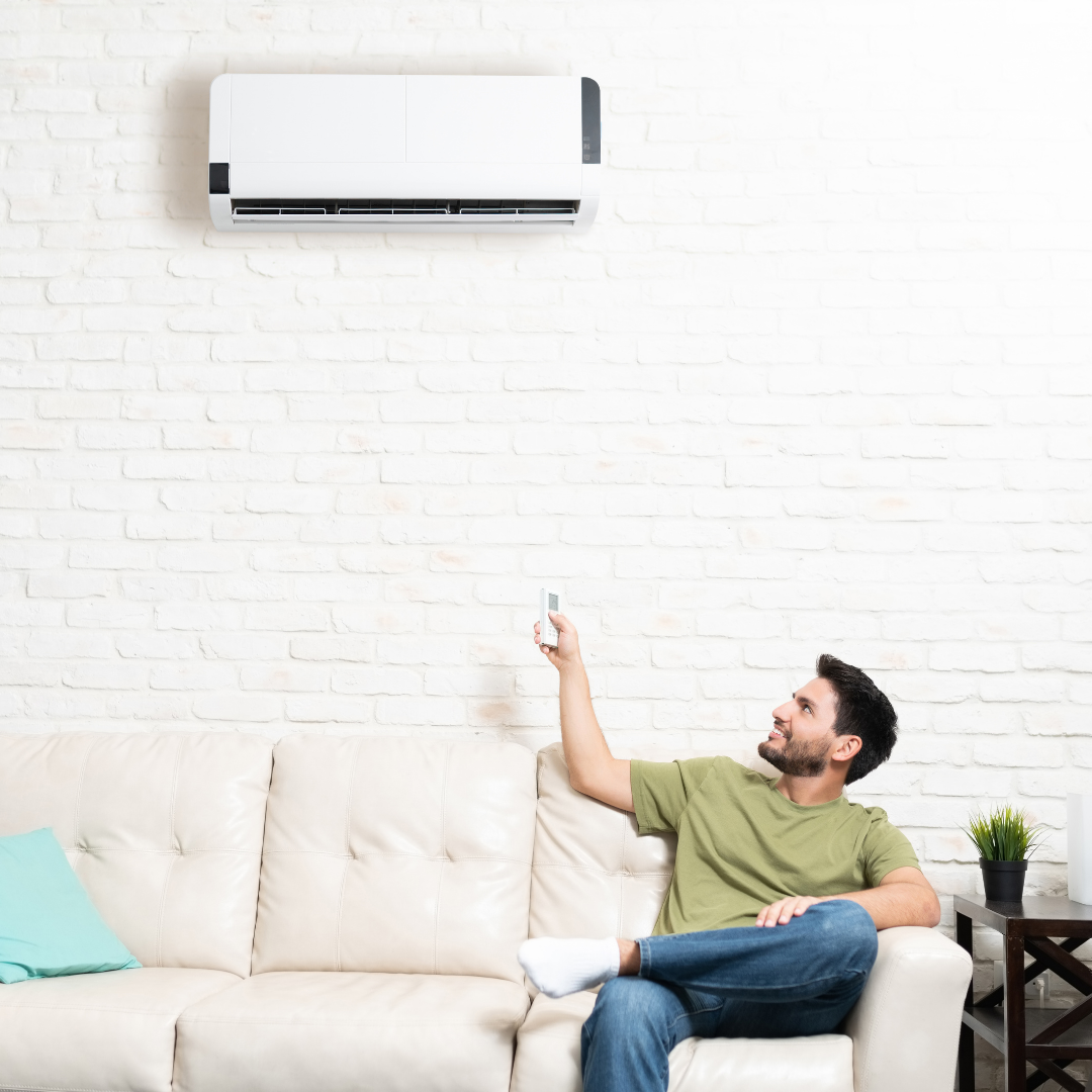 Man sitting on white sofa pointing remote at a mini split wall unit